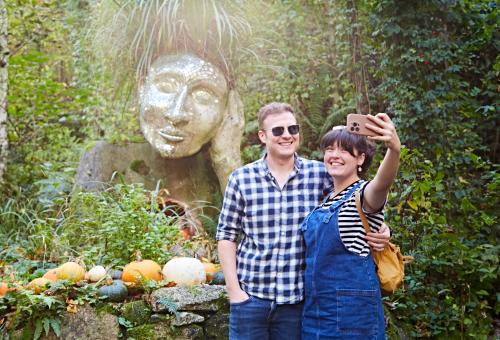 Couple in front of Eve sculpture surrounded by pumpkins taking a selfie